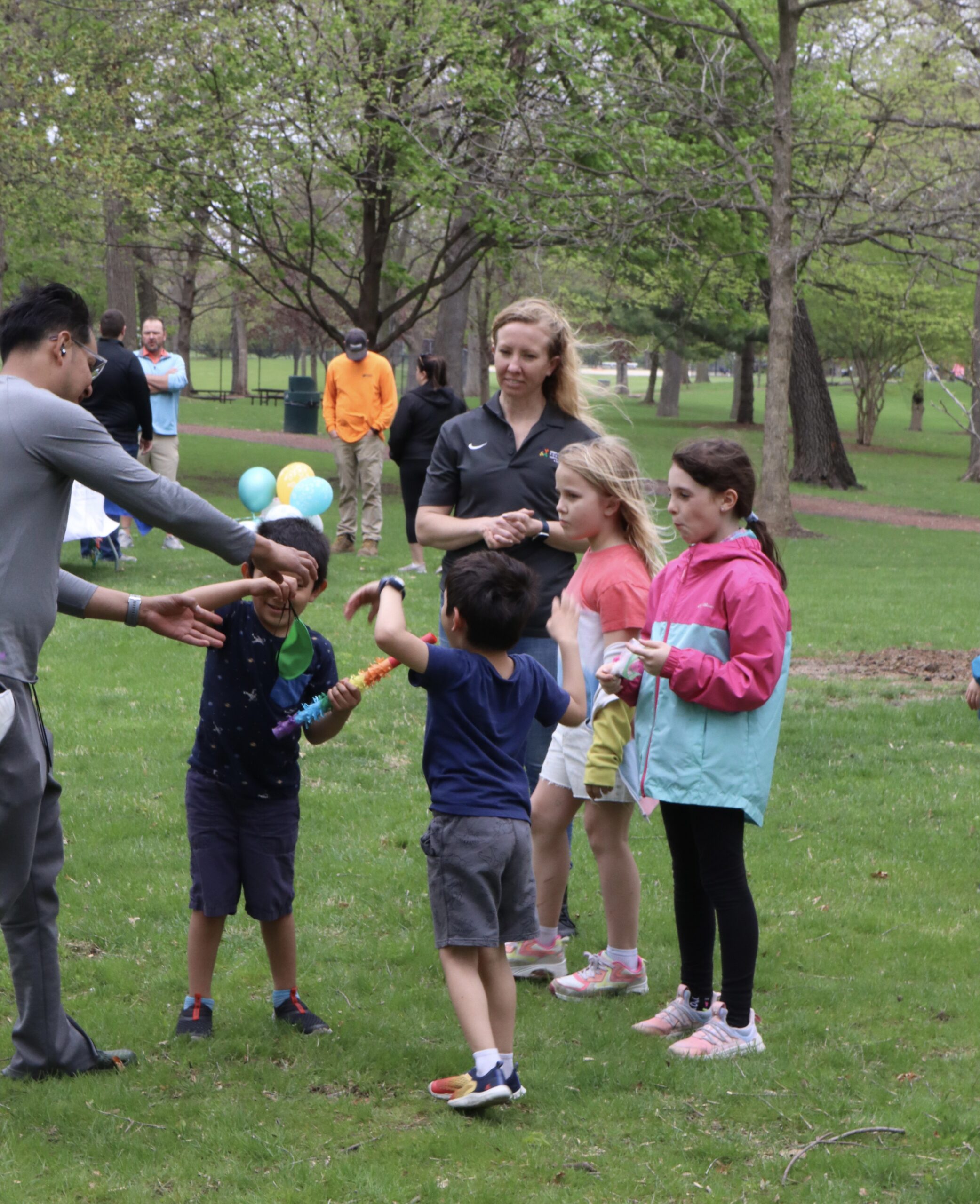 A small group of children and adults are gathered outside on a windy day. They are engaged in a fun family activity.