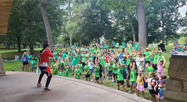 A performer puts on a show for children at the shell in Reed Keppler Park. THere are many children that appear to be dancing along to the music. 