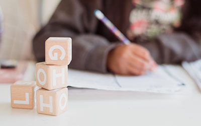 A stock photo of a small child writing with a pencil, with blocks stacked in front.