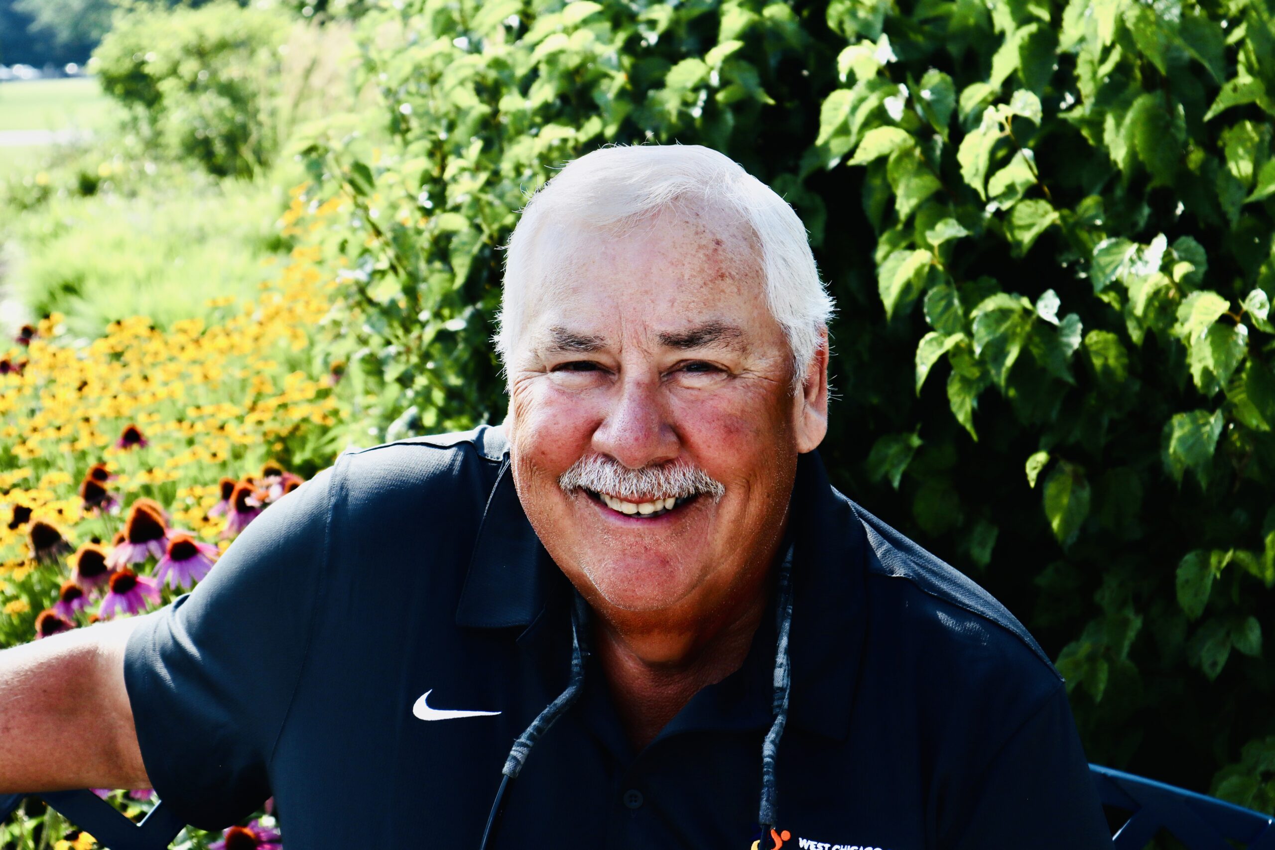 A headshot of Jesse Felix. He is standing outside smiling, wearing a Foundation polo shirt and holding a walking stick.