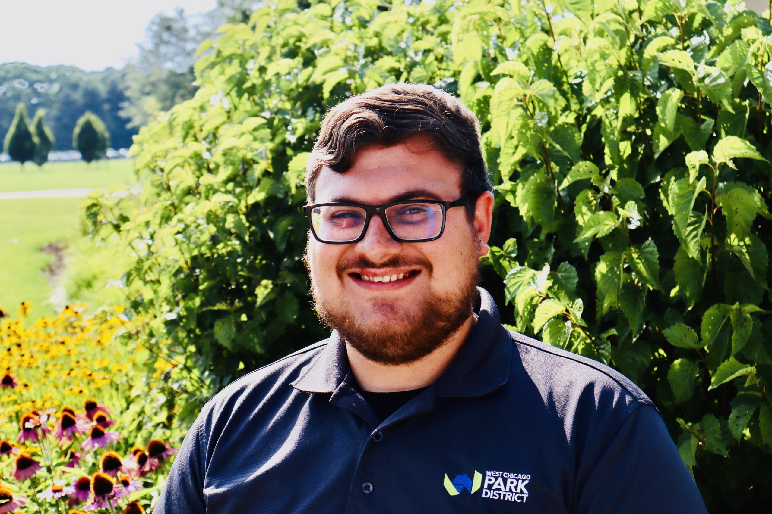 A headshot of Ben Nelson. He is outside wearing a Park District polo shirt. He is wearing glasses and smiling.