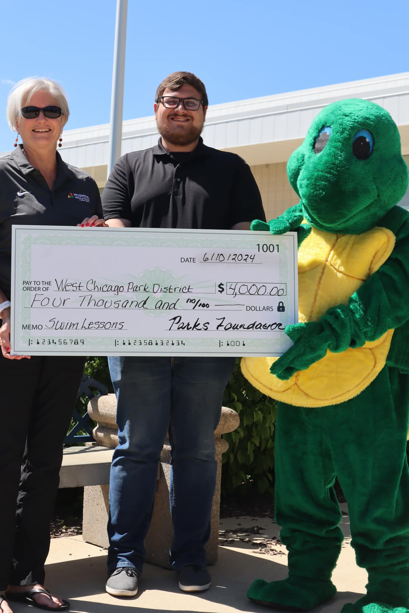 Two Foundation board members are presenting a turtle mascot with a check for $4,000 to sponsor swim lessons for community members