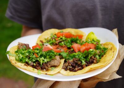 Three street tacos on a paper plate garnished with cilantro and tomato.