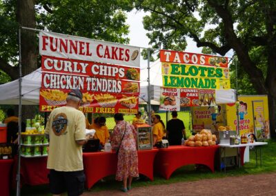 A food vendor advertising all of the food they sell, such as funnel cakes, curly chips, chicken tenders and tacos.