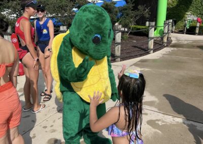 A turtle mascot is giving a small child a high five while at the pool.