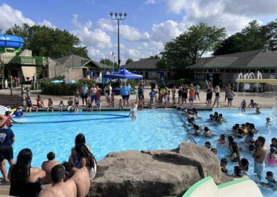 Many people are gathered around a community pool. There is a woman holding a lane in the water while the crowd watches