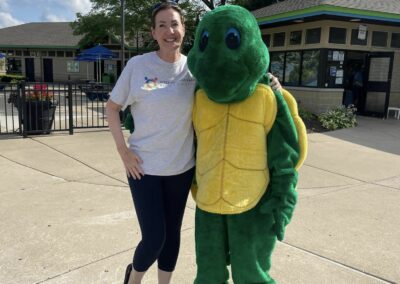 A woman wearing a Parks Foundation t-shirt is posing with a turtle mascot on a sunny day